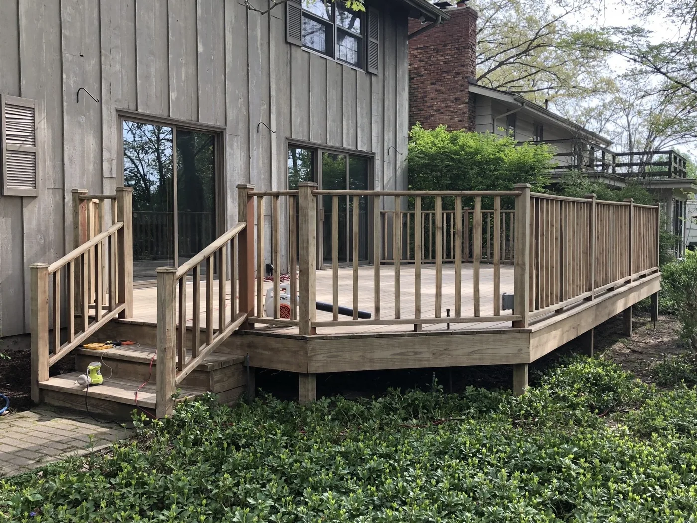 A wooden deck with railings and stairs, attached to the side of a house with light-colored siding and a brick chimney.