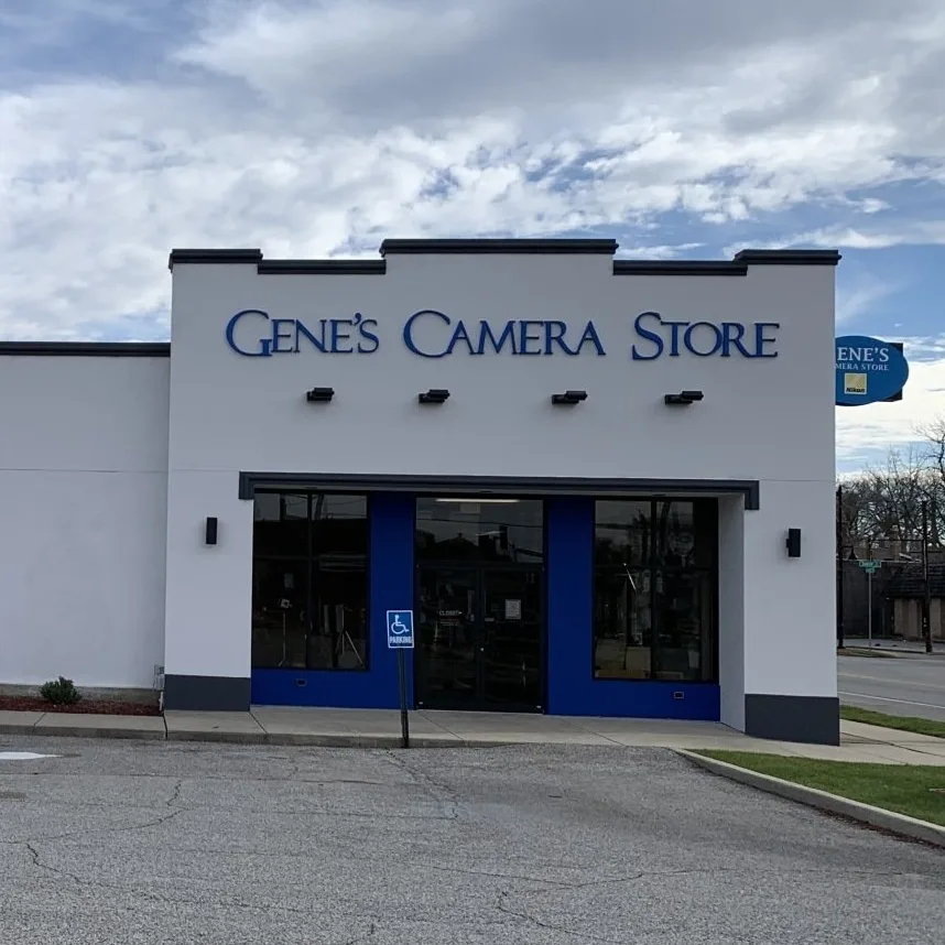 A white building for Gene's Camera Store with a blue entrance and signage under a cloudy sky.
