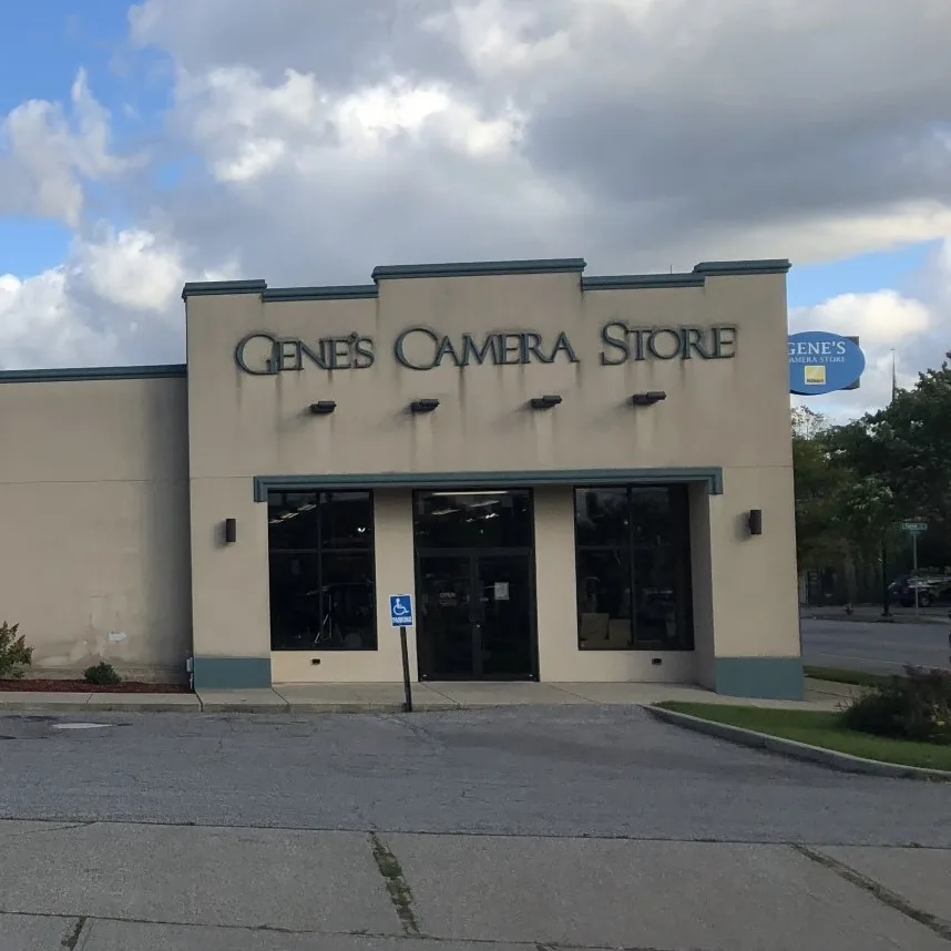 Exterior of Gene's Camera Store, a tan building with large dark windows under a cloudy sky.