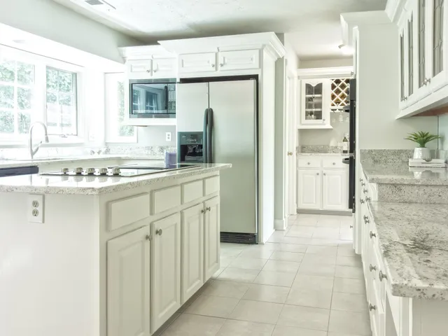 A bright, modern kitchen featuring white cabinets, stainless steel appliances, and a granite-topped kitchen island.