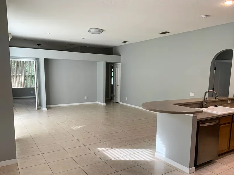 An open-concept living area with gray walls, light tiled floors, and a kitchen island with a stainless steel dishwasher.
