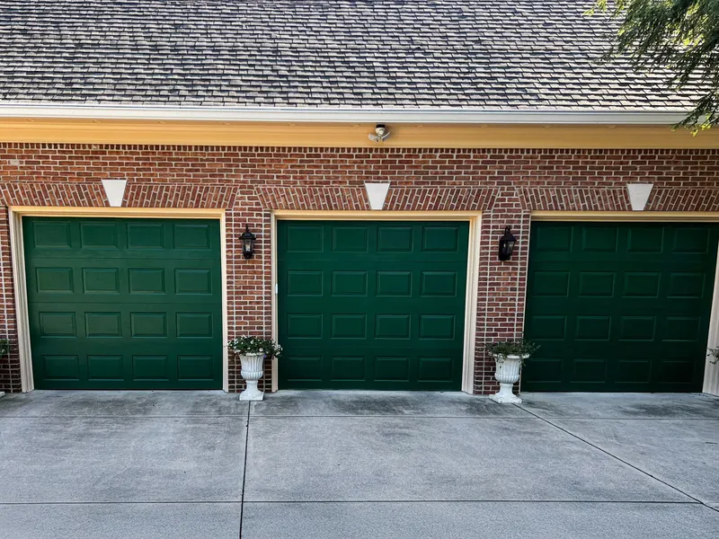 Three green garage doors on a brick house with white planters at the entrance of each bay.