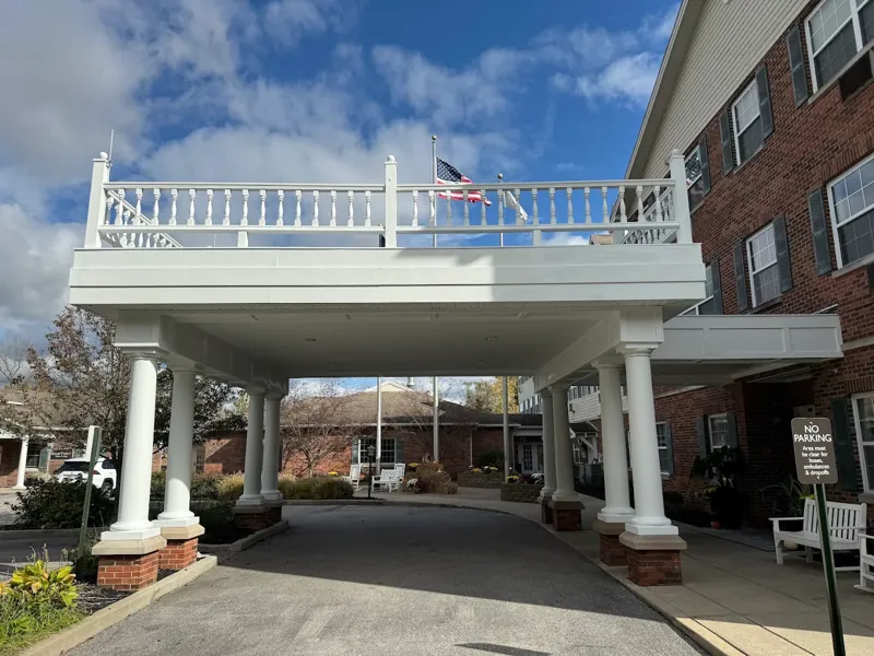 White columned porte-cochere with a balustrade at the entrance of a brick building.
