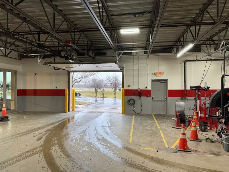 Commercial garage interior with painted gray walls, a red safety stripe, and a sealed concrete floor.