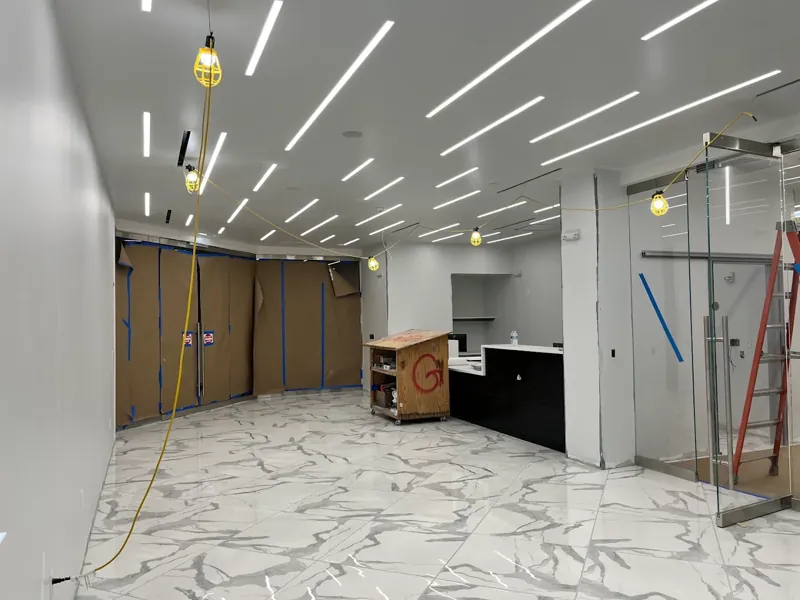 Commercial interior under renovation with white walls, linear LED lighting, and marble-look floors.