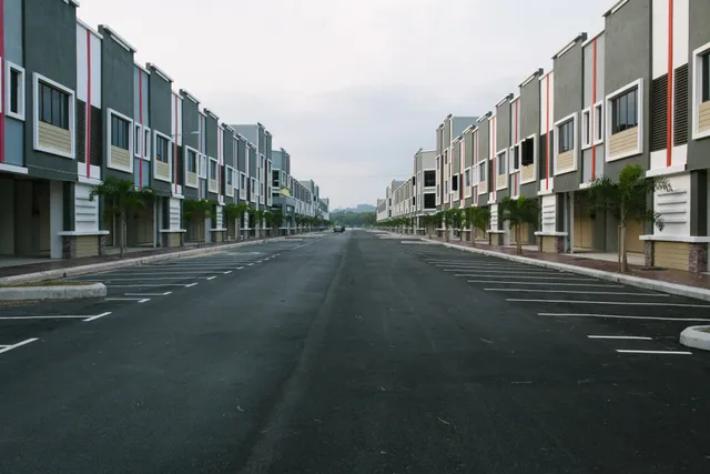 A symmetrical perspective view of a newly paved road flanked by rows of modern, gray-toned townhouse buildings.