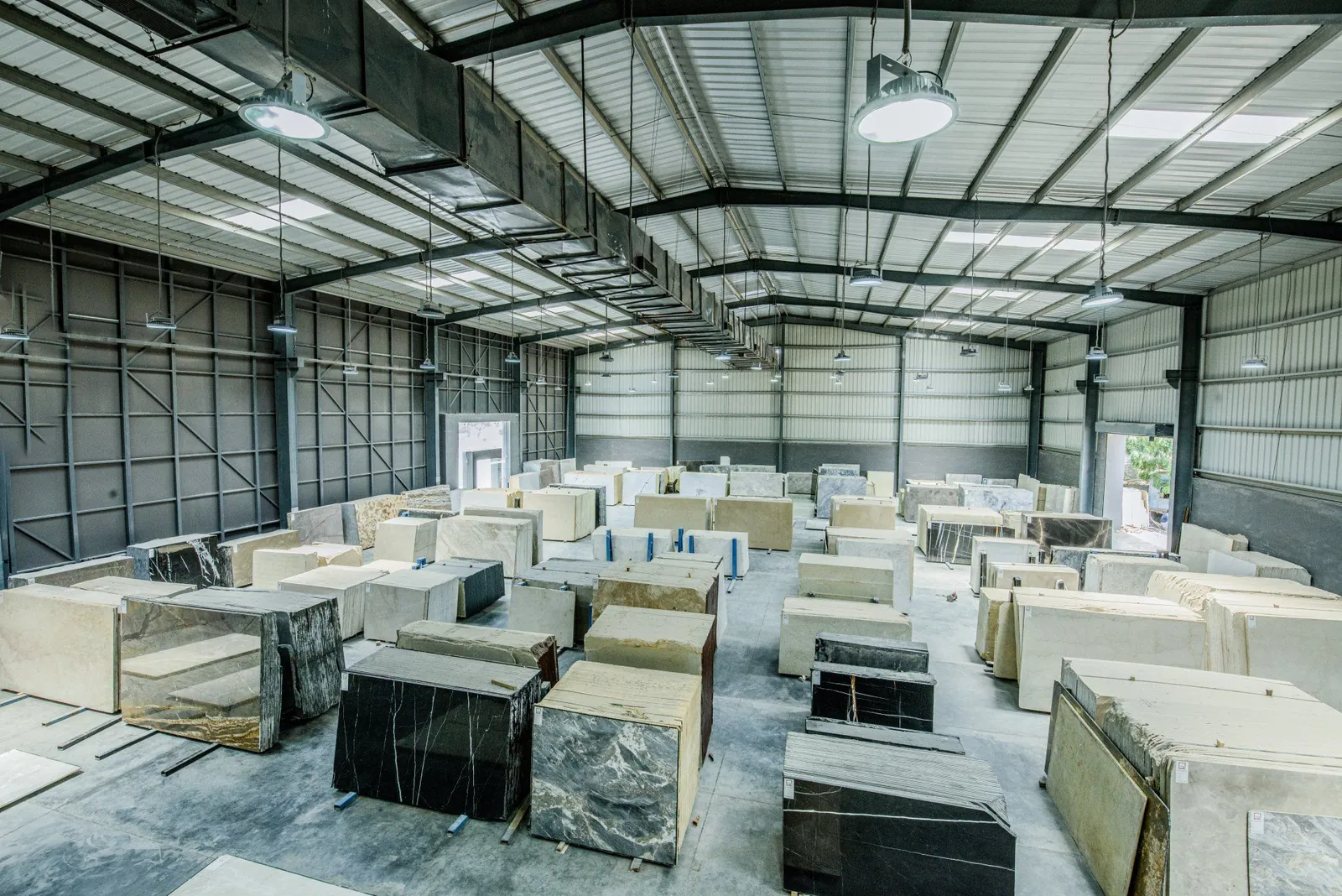 A large warehouse filled with numerous rectangular slabs of natural stone, organized in rows on a concrete floor.
