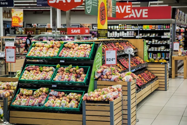Produce section in a grocery store featuring neatly stacked wooden crates filled with various fruits and vegetables.