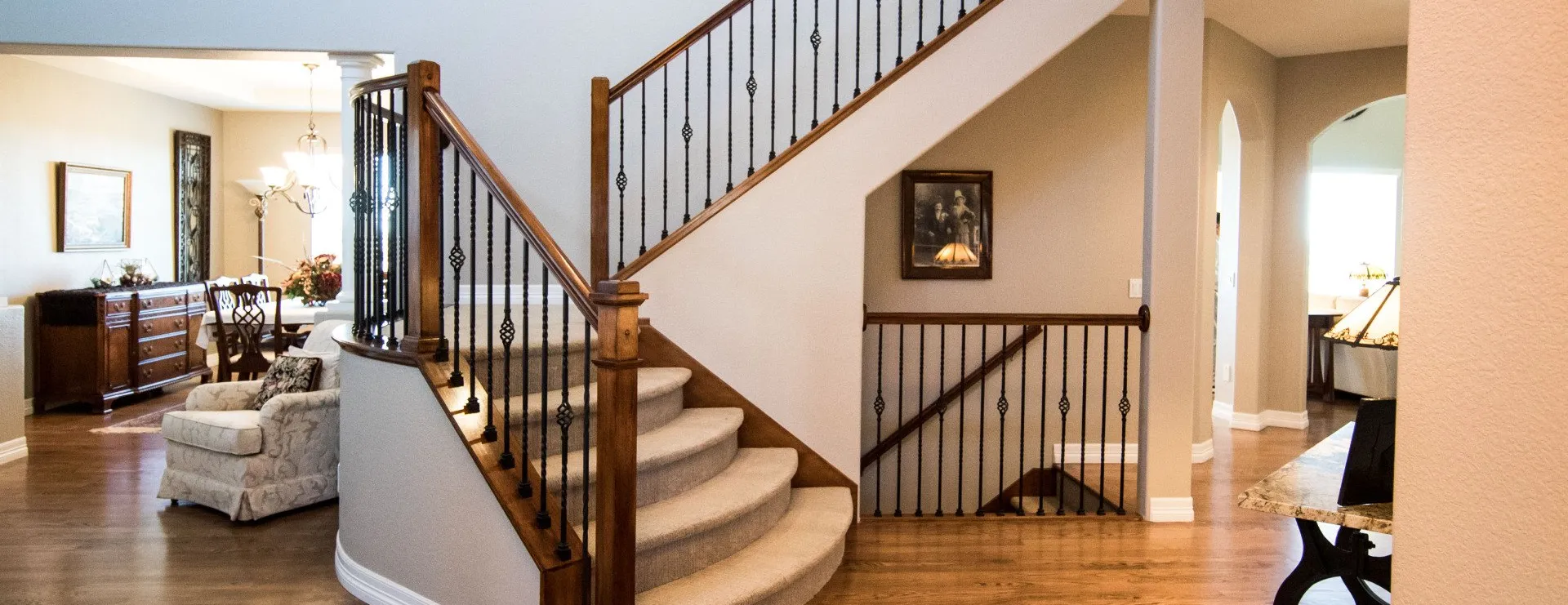 A grand staircase with carpeted steps and wooden railings in a spacious, neutrally toned residential entryway.