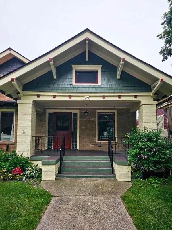 A single-story Craftsman-style bungalow with a tan brick base, dark green siding in the gable, and a covered front porch.